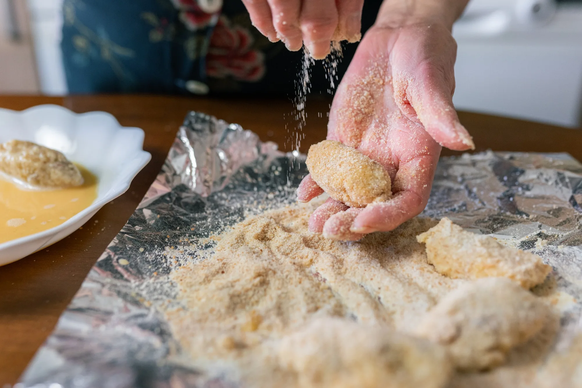 Senior woman coating croquettes with breadcrumbs at home